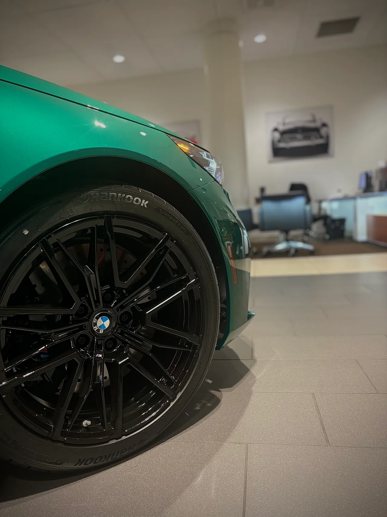 Black wheel and front fender of a green sedan inside a showroom