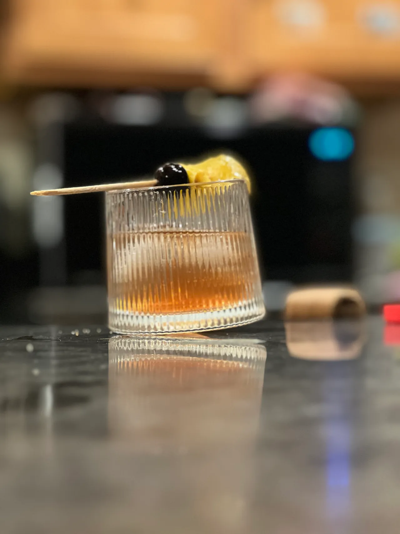 Old fashioned cocktail with cherry and citrus garnish on a reflective bar top